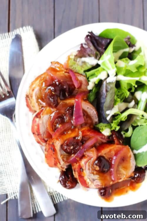 Maple Bacon-Wrapped Pork Tenderloin with Rosemary Cherry Sauce | gimmesomeoven.com Close-up of Maple Bacon-Wrapped Pork Tenderloin slices drizzled with Rosemary Cherry Sauce, garnished with fresh rosemary.