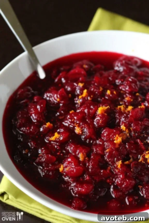 A close-up shot of the glistening Orange Bourbon Cranberry Sauce, showcasing its rich texture and color, adorned with fresh orange zest.