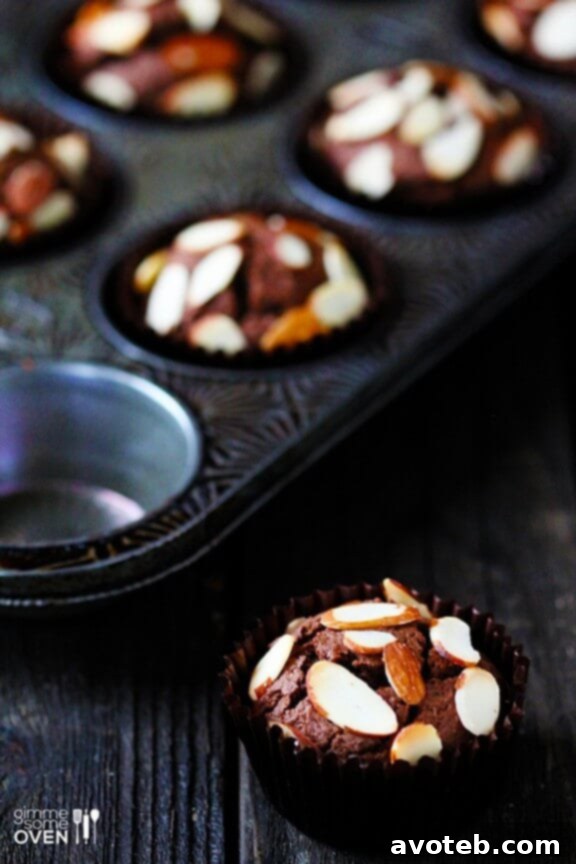 A tray of freshly baked Chocolate Almond Muffins, golden brown and topped with almonds.