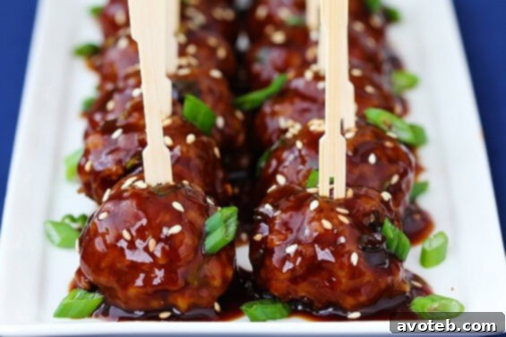 Saucy Asian Meatballs, glistening with a sweet and savory glaze, garnished with sesame seeds and green onions.