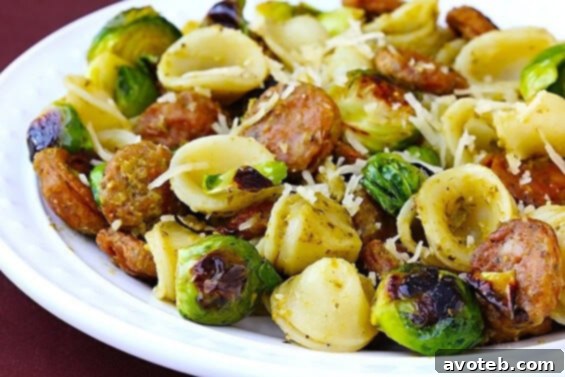 A plate of Pesto Pasta with Chicken Sausage and Roasted Brussels Sprouts, topped with Parmesan cheese.