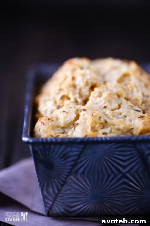 Close-up of a slice of Whole Wheat Garlic & Herb Beer Bread on a wooden cutting board.