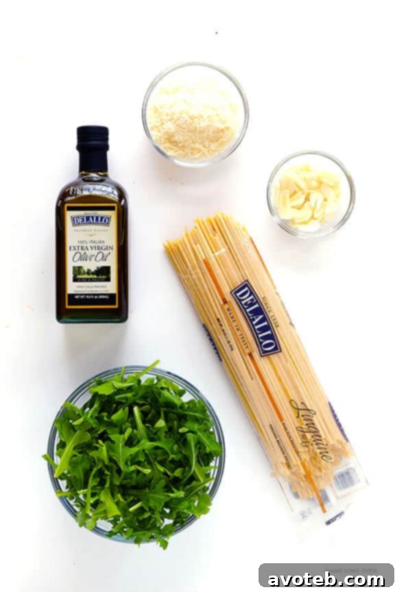 Five core ingredients: olive oil, arugula, pasta, Parmesan, and garlic, laid out on a wooden surface