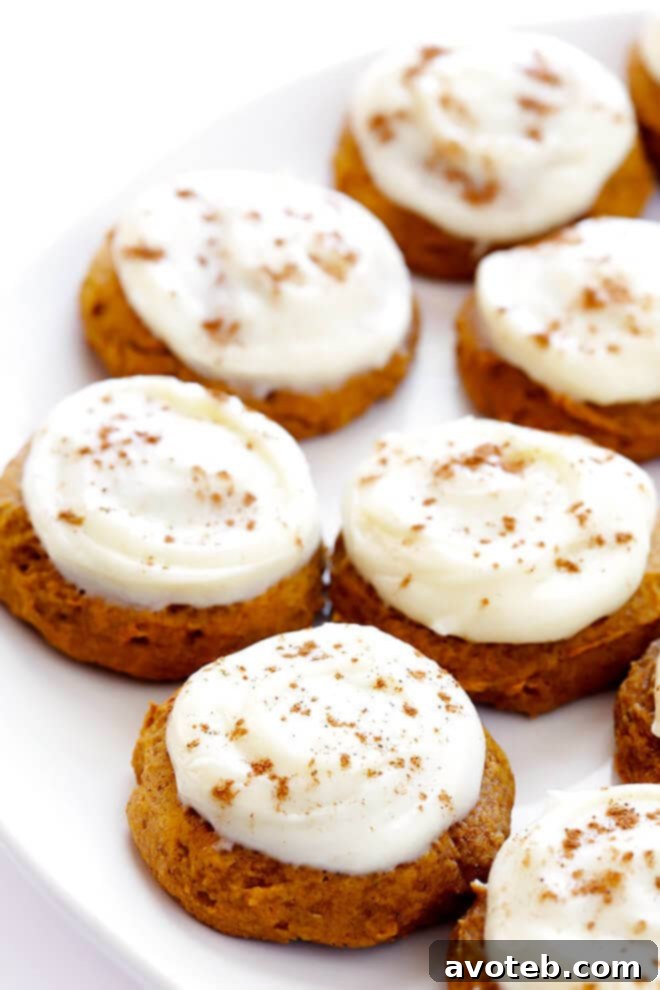 A soft pumpkin cookie being frosted with a generous swirl of cream cheese icing, ready for its final garnish.