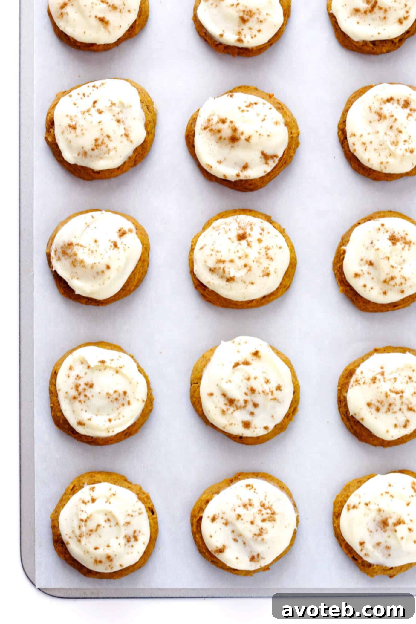 A beautiful close-up of several iced pumpkin cookies stacked on a white plate, garnished with a sprinkle of spice.