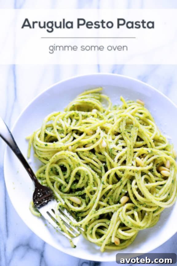 Cooked pasta being tossed with vibrant green arugula pesto.