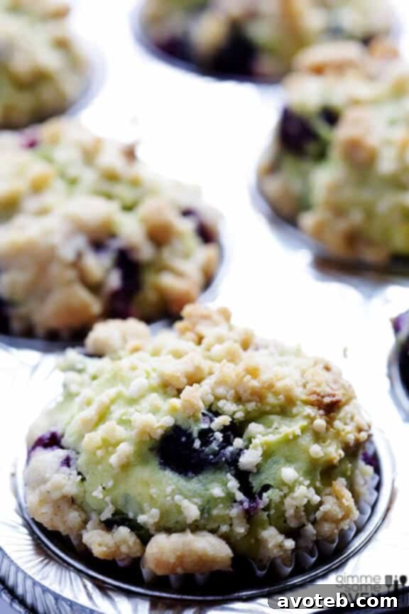 A close-up of a single blueberry avocado muffin, showcasing its perfectly golden-brown streusel topping and the vibrant blueberries.