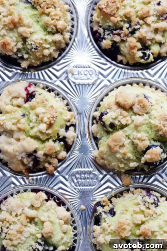 A stack of golden-brown blueberry avocado muffins with a delicate crumble topping, presented on a light background.