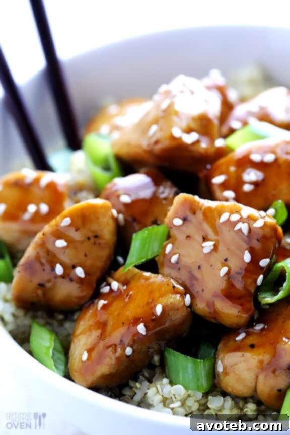 Close-up of lighter sesame chicken pieces with green onions, served on a plate next to quinoa. Emphasizes the fresh ingredients and appetizing presentation of the healthy meal.