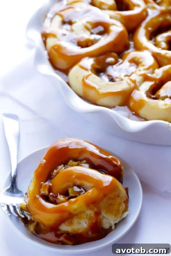 Hand pulling apart a caramel apple cinnamon roll, revealing the soft, fluffy interior.