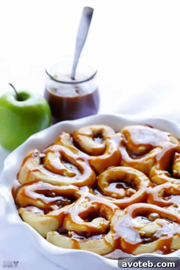 Close-up of a single Caramel Apple Cinnamon Roll, showcasing the golden-brown crust, visible apple chunks, and swirling caramel glaze.