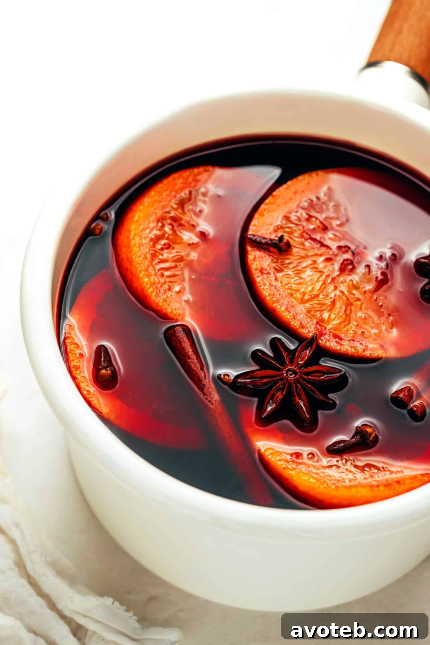 A saucepan filled with simmering mulled wine, rich with red wine, orange slices, and whole spices, ready for infusing flavors.