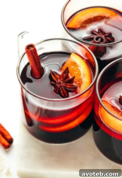 A beautifully composed shot of mulled wine in a glass mug, garnished with citrus and spices, beside an open cookbook.