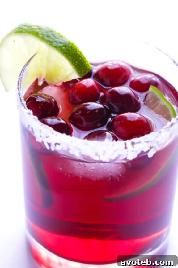 A hand stirring a pitcher of Cranberry Margaritas, showing the vibrant mixture before serving.