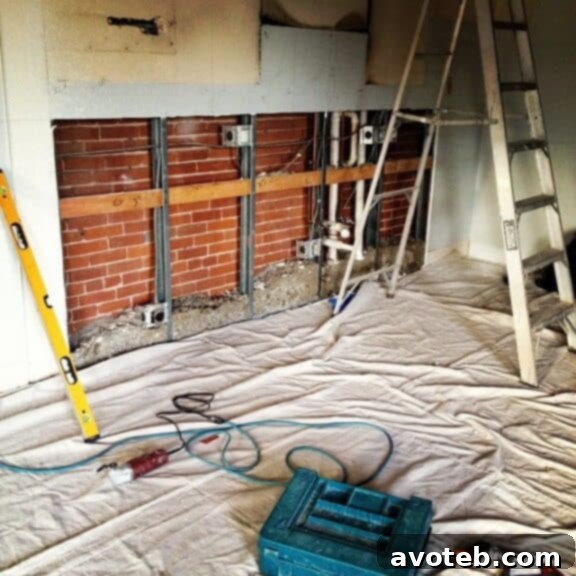 Kitchen during renovation with some cabinets installed, showing exposed wiring and plumbing.