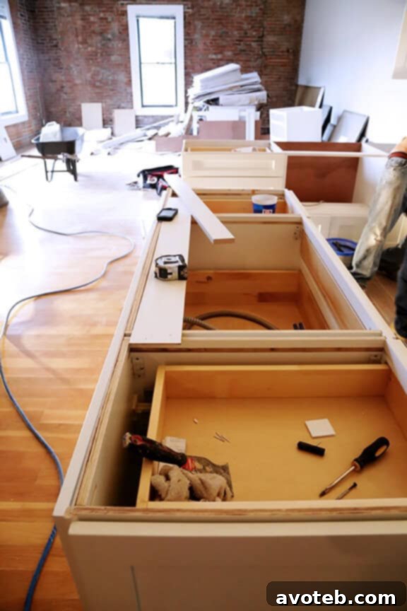 A growing pile of cabinet boxes in the background of the kitchen remodel, illustrating the sheer volume of components.