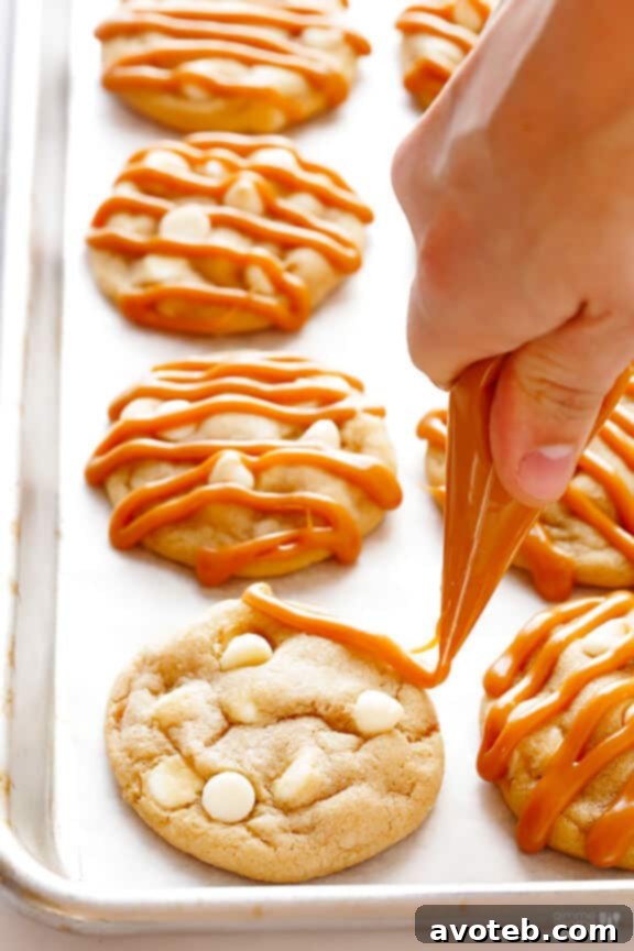 Caramel Drizzle for the Ultimate Cookie Experience A plate of Caramel White Chocolate Cookies generously drizzled with rich caramel sauce.