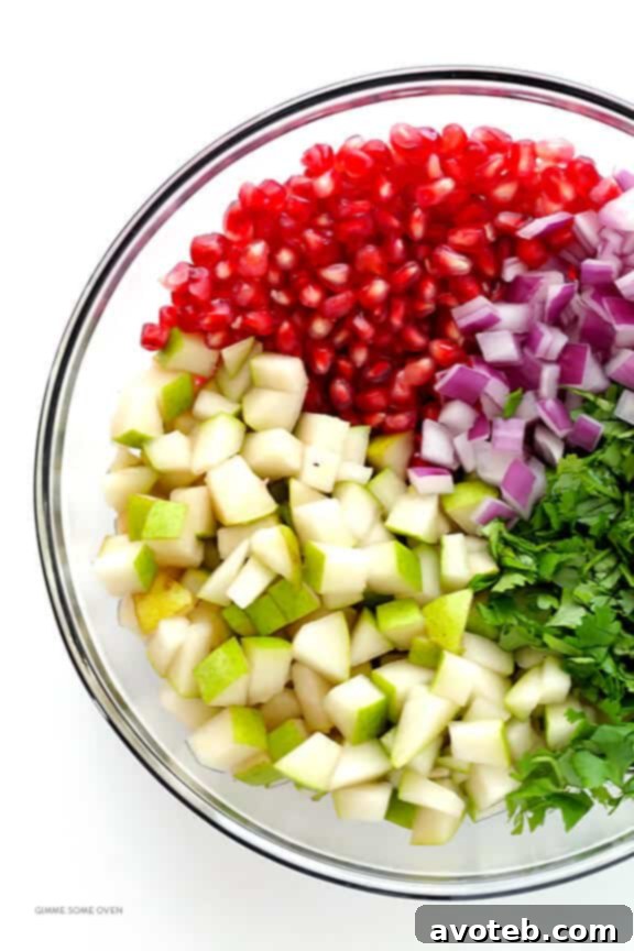 A shot from above showcasing the fresh, colorful ingredients for the salsa laid out: diced pears, pomegranate seeds, chopped cilantro, and sliced red onion, ready for mixing.