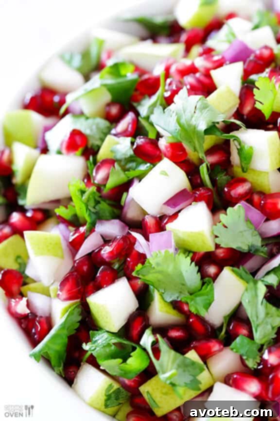 A close-up of a serving spoon scooping out a generous portion of the Pear Pomegranate Salsa, demonstrating its fresh and chunky texture, perfect for dipping.