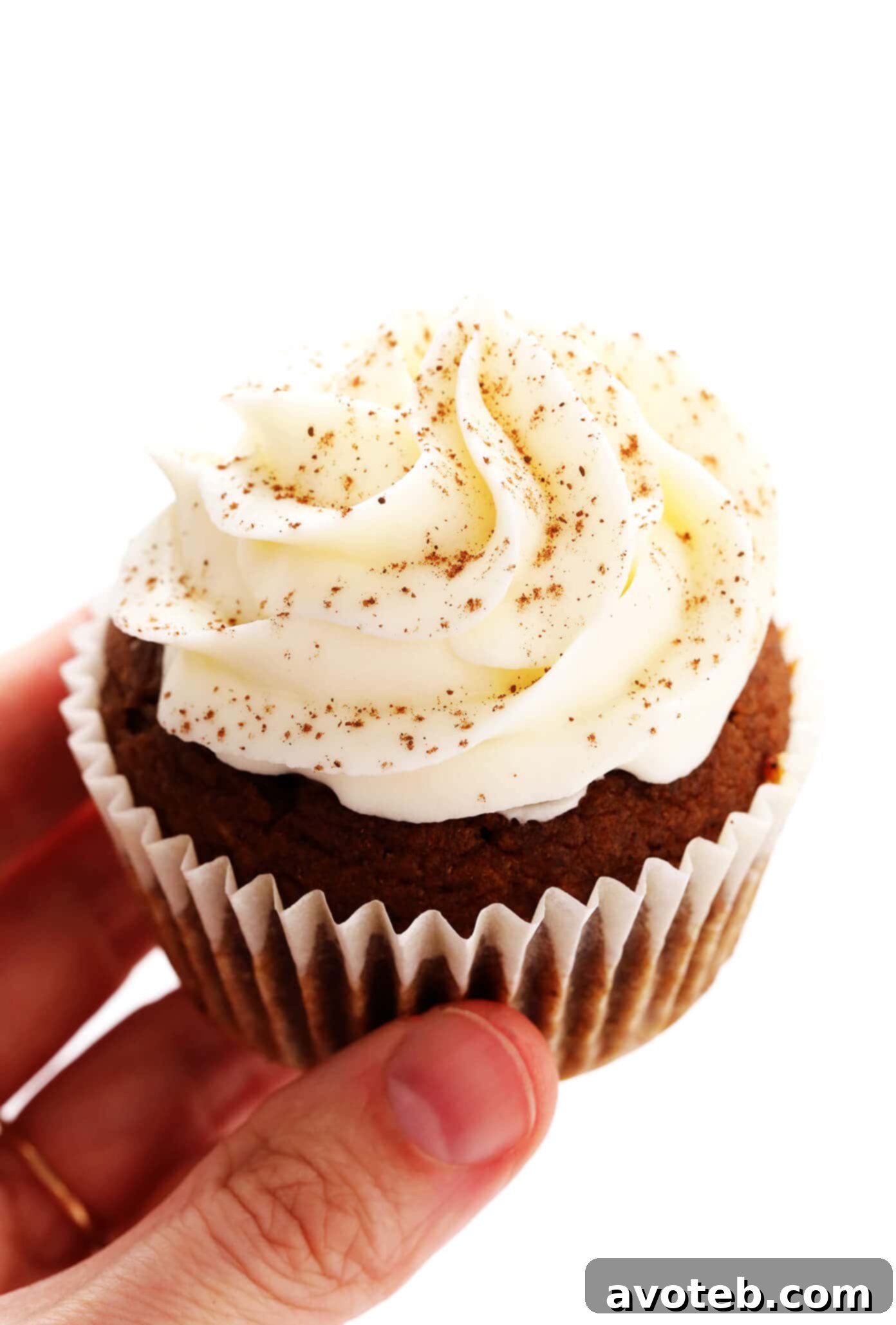 Close-up shot of a hand holding a single pumpkin cupcake, showcasing the thick layer of cream cheese frosting.
