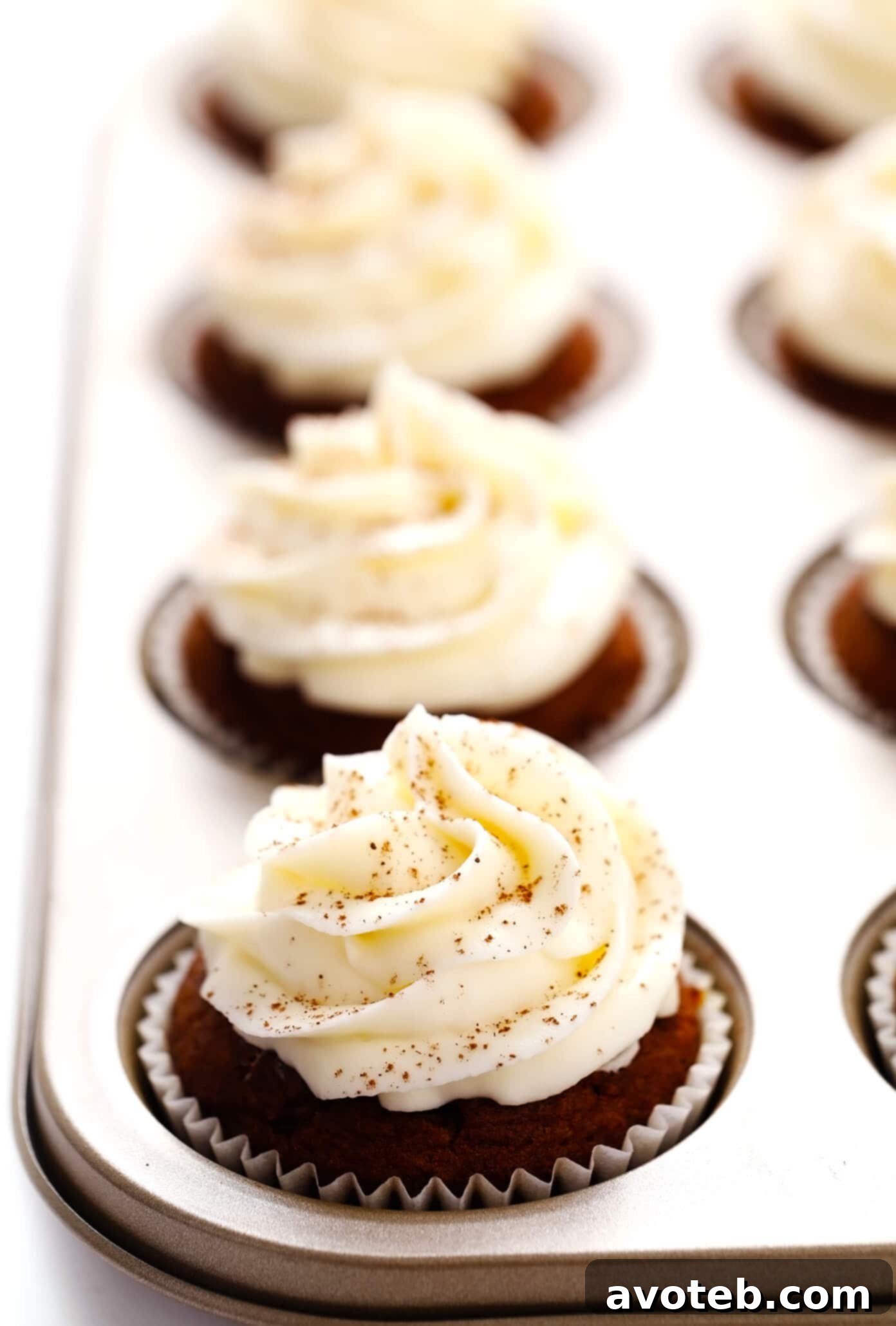 Freshly baked pumpkin cupcakes with cream cheese frosting arranged in a muffin pan.