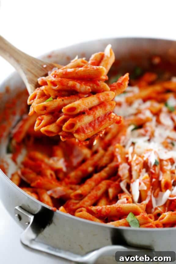 A bowl of pasta with roasted red pepper sauce and a fork.