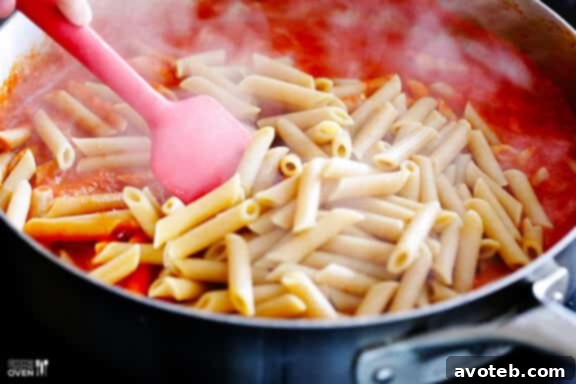 Al dente pasta being added to the simmering red pepper sauce.