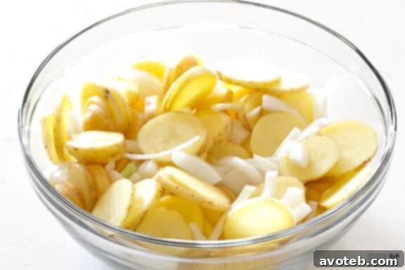 Sliced potatoes, onions, and garlic in a large mixing bowl