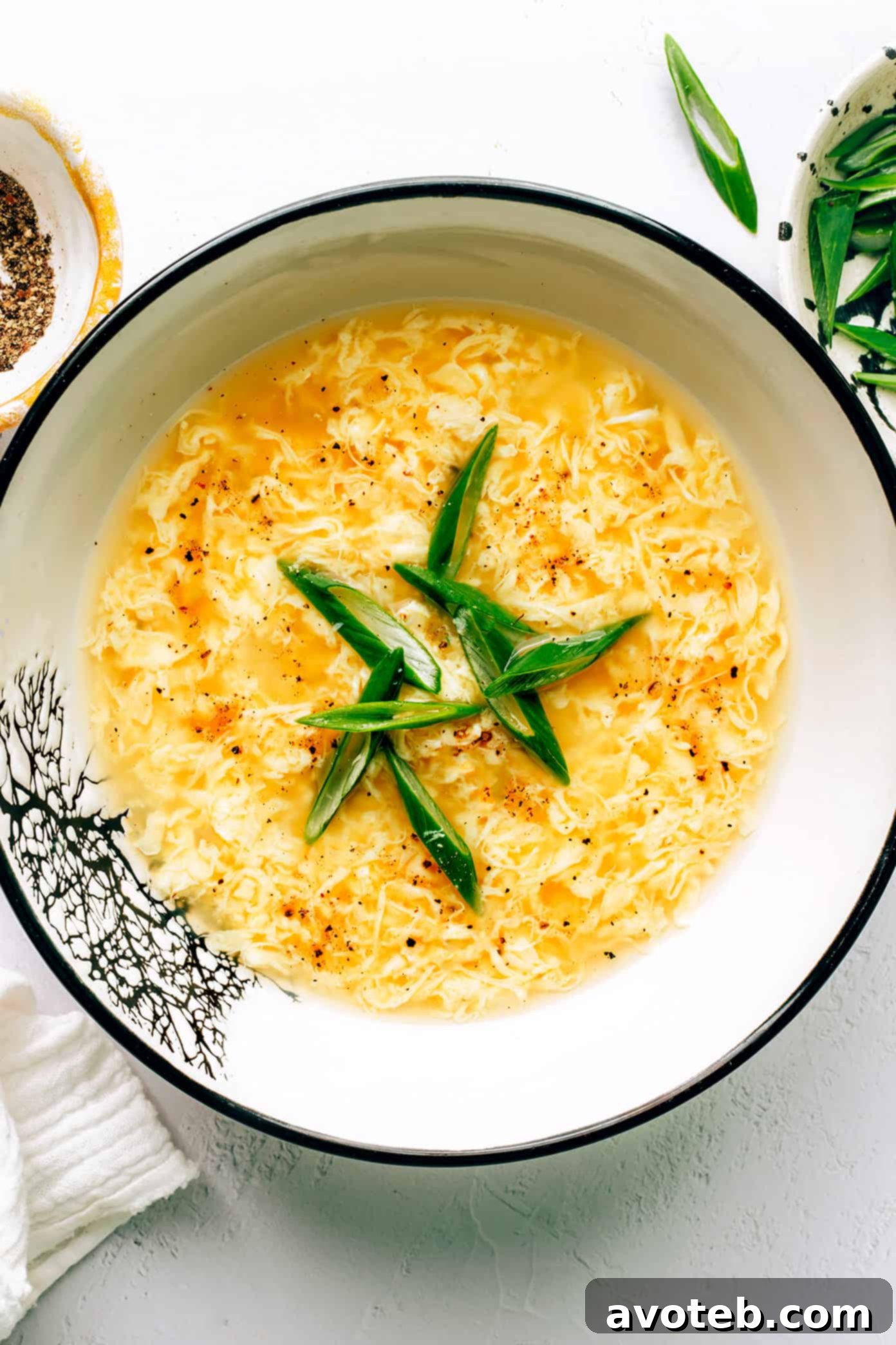 A bowl of freshly made egg drop soup, garnished with green onions, sits on a rustic wooden surface, with a spoon ready for tasting.