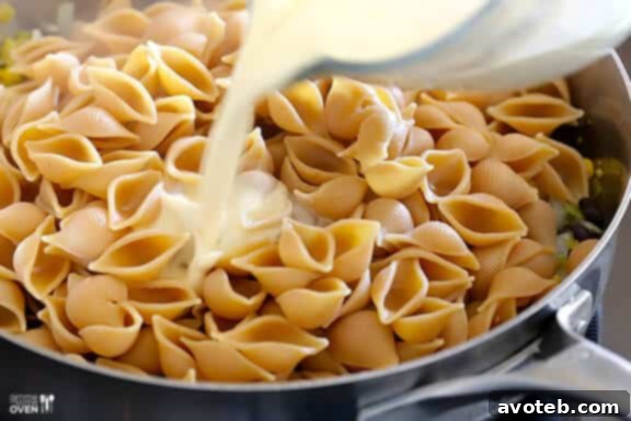 Creamy sauce being poured over pasta and vegetables