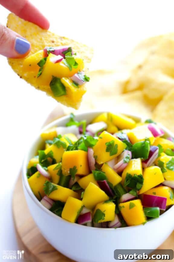 This 5-ingredient fresh mango salsa recipe is easy to make and tastes fantastic as a dip with chips or as a versatile topping on Mexican dishes. A bowl of homemade 5-Ingredient Mango Salsa with a serving spoon, showcasing its chunky texture and fresh ingredients