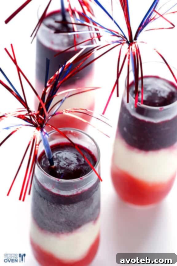 Three Red, White & Blue(berry) Margaritas in tall glasses, garnished with small American flag picks, on a rustic wooden surface, ideal for a patriotic party. #margaritarecipe #cocktail