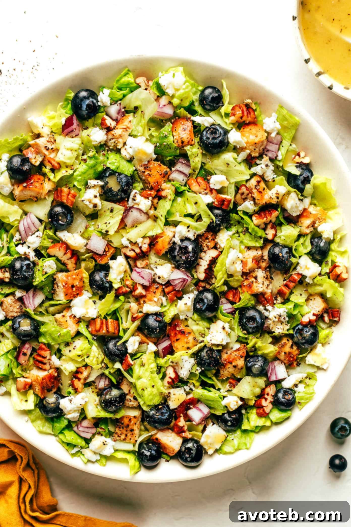 Close-up of the Blueberry Chicken Chopped Salad in a bowl, with a drizzle of lemon vinaigrette being added, showcasing the vibrant colors and fresh ingredients.