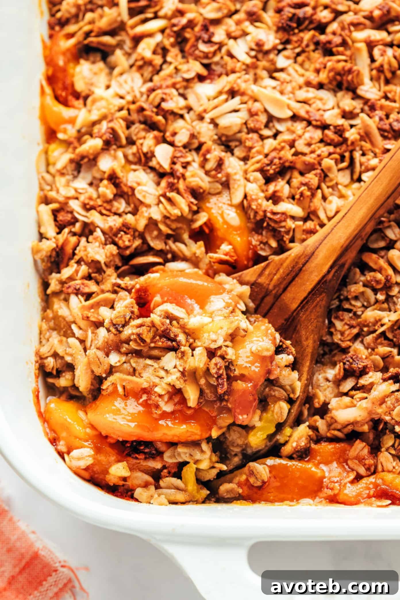 A close-up shot of the ginger peach crisp in a bowl, with a spoon scooping out a portion, highlighting the texture.