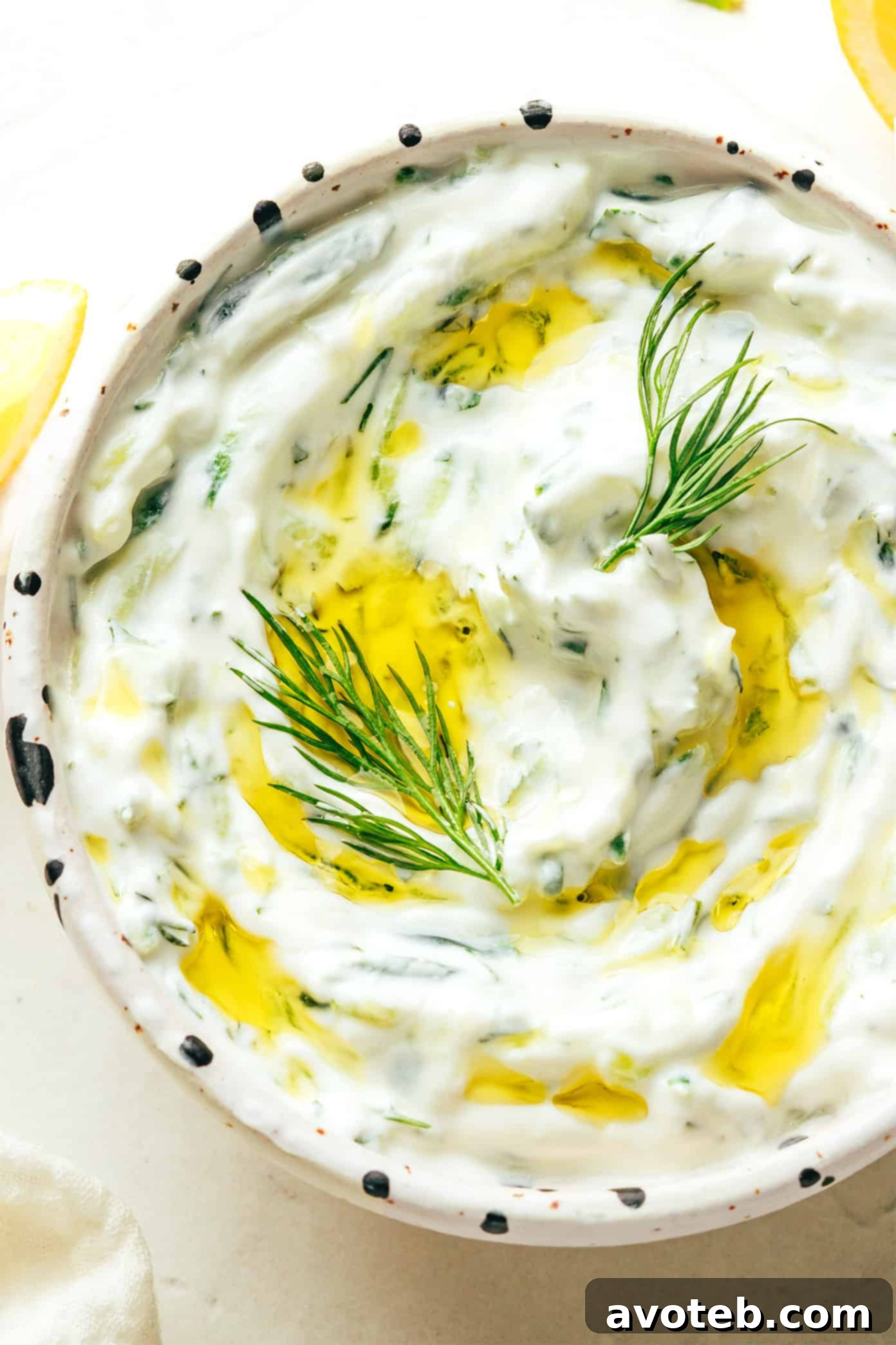Close-up of a hand serving fresh Tzatziki into a small bowl, highlighting its creamy texture.
