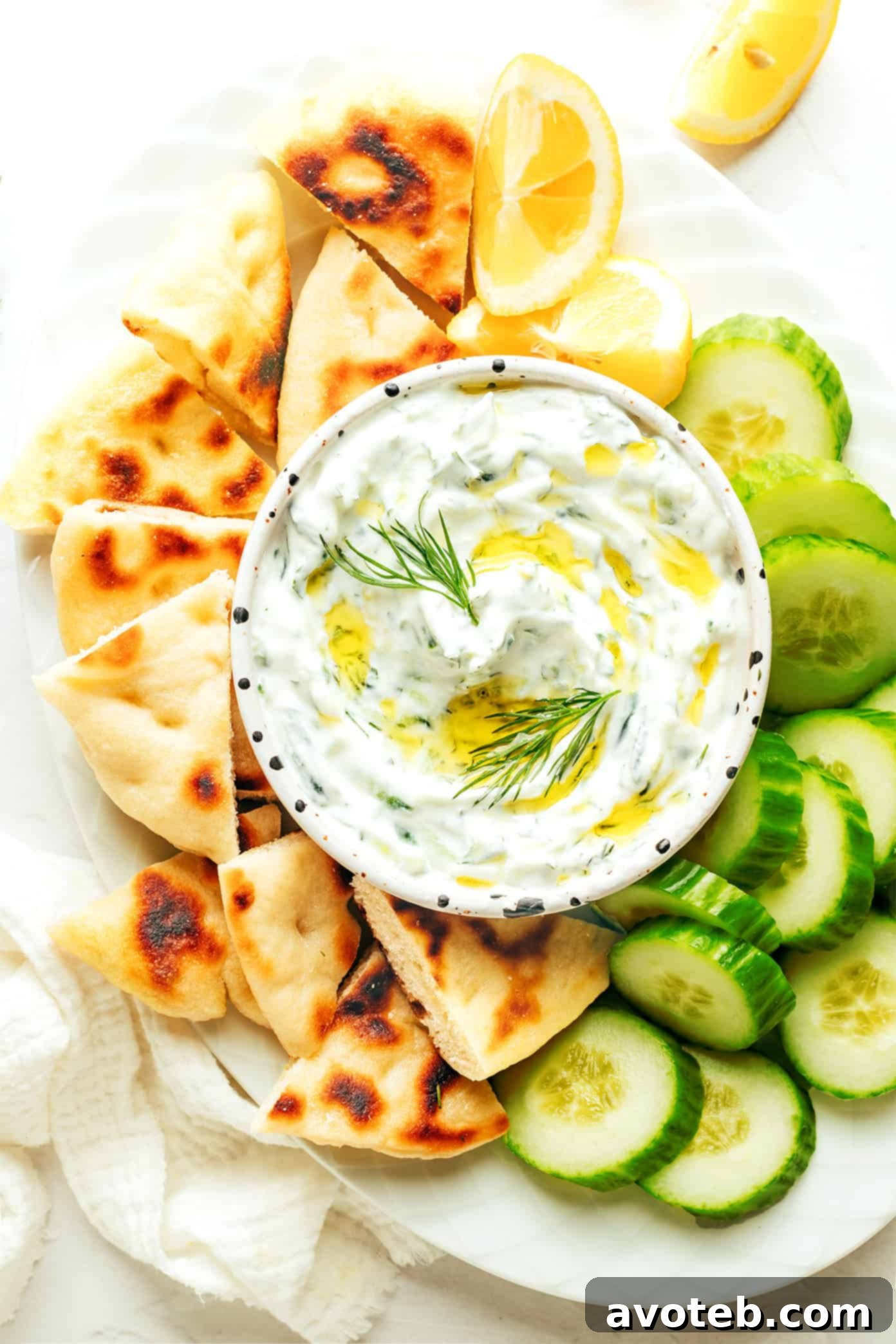 A spread of various Greek dishes, including a generous bowl of Tzatziki, pita bread, and grilled vegetables, perfect for sharing.