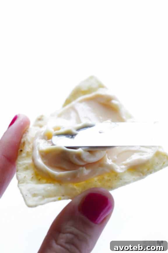 Hands spreading The Laughing Cow cheese on a tortilla chip.