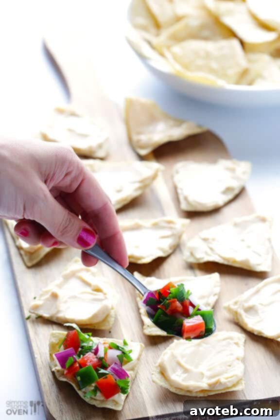 Pico de gallo being spooned onto a cheese-covered tortilla chip.