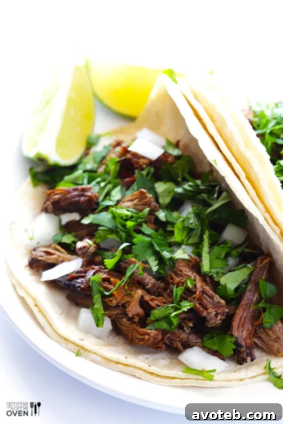 Tender, slow-cooked beef barbacoa, perfect for tacos and burritos, served on a plate with fresh cilantro and lime wedges.