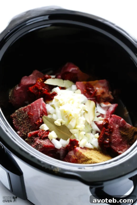 Close-up shot of shredded barbacoa beef simmering in its flavorful juices within a slow cooker, showcasing its rich texture.