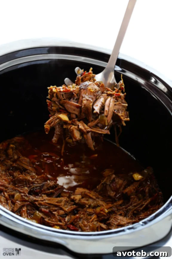 Two forks expertly shredding a large piece of cooked beef chuck roast, demonstrating the tenderness achieved in the slow cooker.