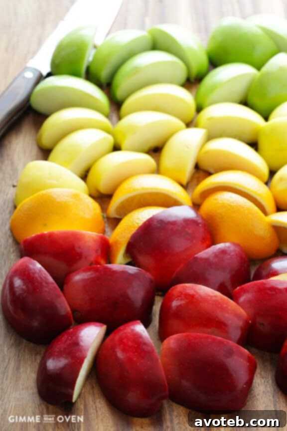An array of fresh, vibrant apples and a whole orange, essential ingredients laid out for making delicious homemade apple cider.