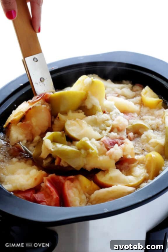 The interior of a slow cooker, brimming with chopped apples, orange slices, and whole spices, gently simmering to create fragrant apple cider.