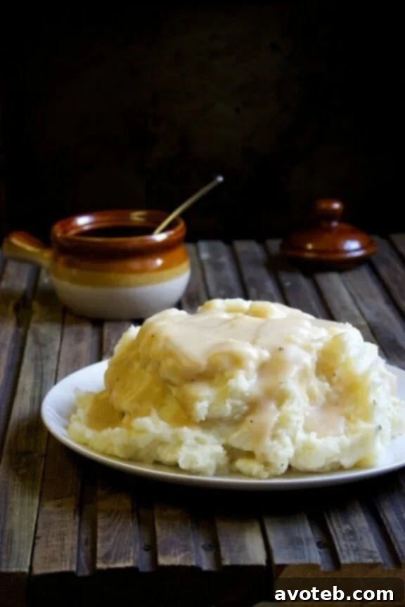A beautiful serving bowl overflowing with exceptionally creamy, smooth mashed potatoes, with a ladle of rich, glistening brown gravy being poured over them, signifying ultimate comfort food.