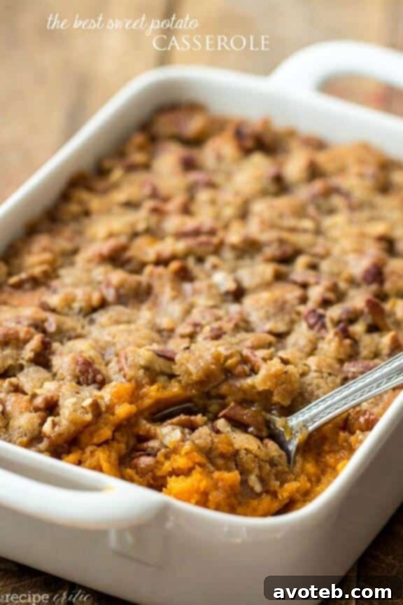 A bubbling, golden-brown Sweet Potato Casserole baked in a casserole dish, topped with a crunchy pecan streusel, with some portions scooped out ready for serving.
