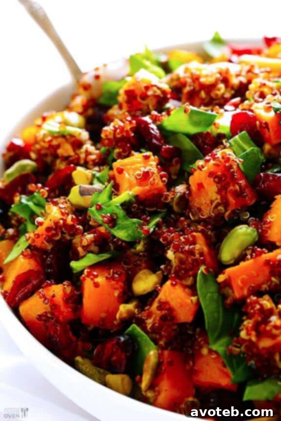 A close-up image of a vibrant Quinoa "Stuffing" dish, featuring fluffy quinoa mixed with golden roasted butternut squash cubes, bright red dried cranberries, and green pistachios, artfully garnished with fresh herbs, ready to be served.
