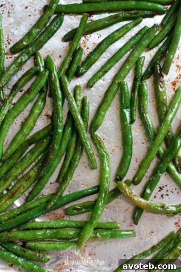A vibrant platter of perfectly roasted green beans, glistening with olive oil, showing a slight char, and generously sprinkled with grated Parmesan cheese, ready for serving.