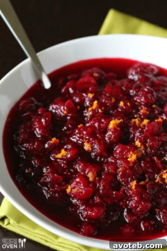A rustic bowl of homemade Orange Bourbon Cranberry Sauce, showcasing its rich, deep red color and chunky texture, garnished with fresh orange slices and vibrant cranberries.