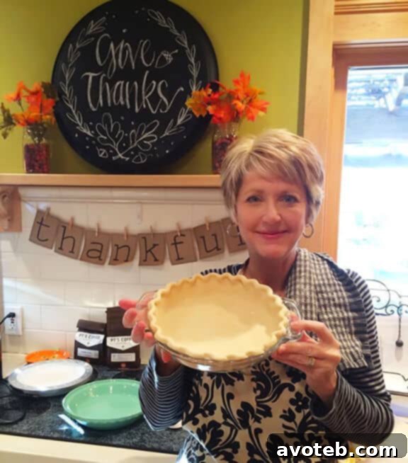 A baker's hands gently crimping the edge of a golden pie crust in a metal pie dish, demonstrating a beautiful, non-shrunken result.