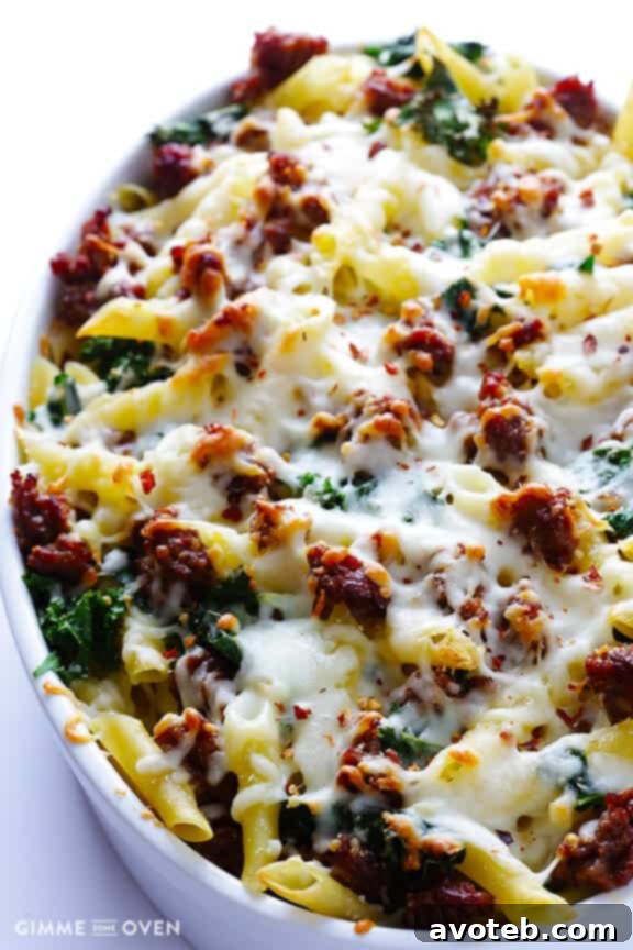 Layered baked ziti with pasta, sausage, kale, and mozzarella cheese in a baking dish before baking.
